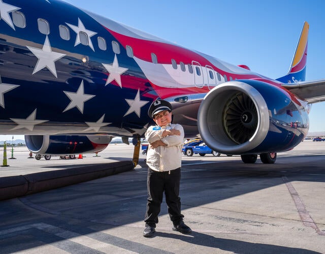 Boy standing in front of an airplane wearing a pilot uniform 