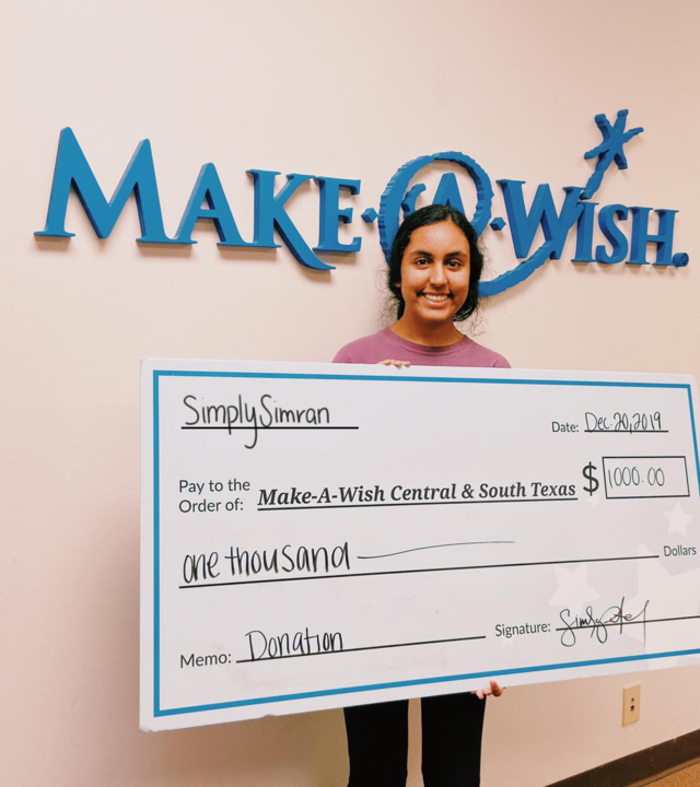 Simran holding a big check make out to Make-A-Wish CSTX for $1,000