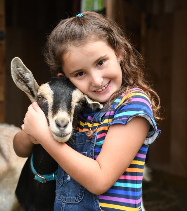 7-year-old Aynsly hugs a baby goat and smiles