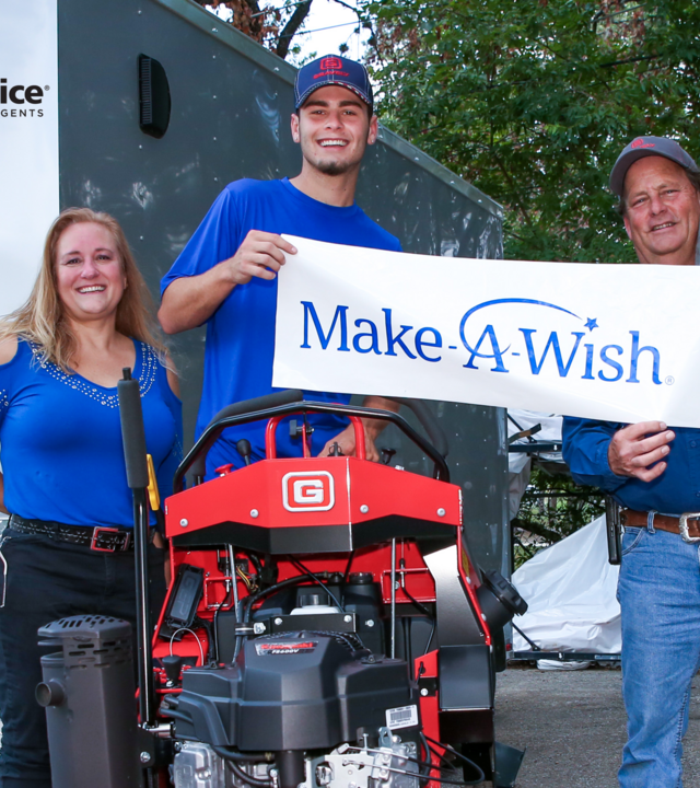 Mason with mom and company rep holding Make-A-Wish sign standing on red lawnmower.