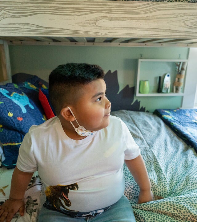 wish boy Zabdiel sitting on his dinosaur-themed bed