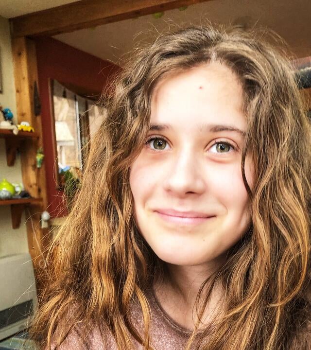 A young woman with wavy brown hair smiles