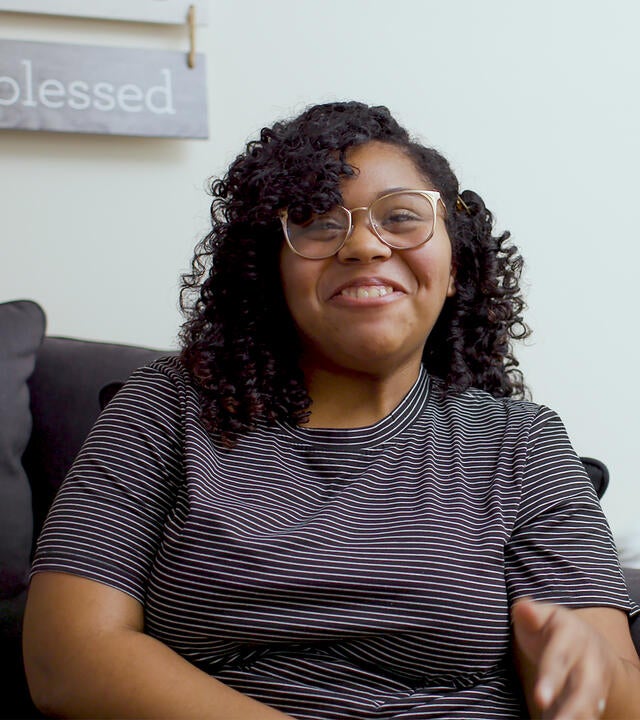 Chairalis, sitting in her living room in gray tshirt