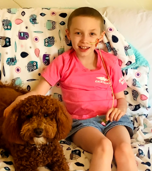 Wish kid Eleanor sitting on her bed with her goldendoodle puppy, Willow.