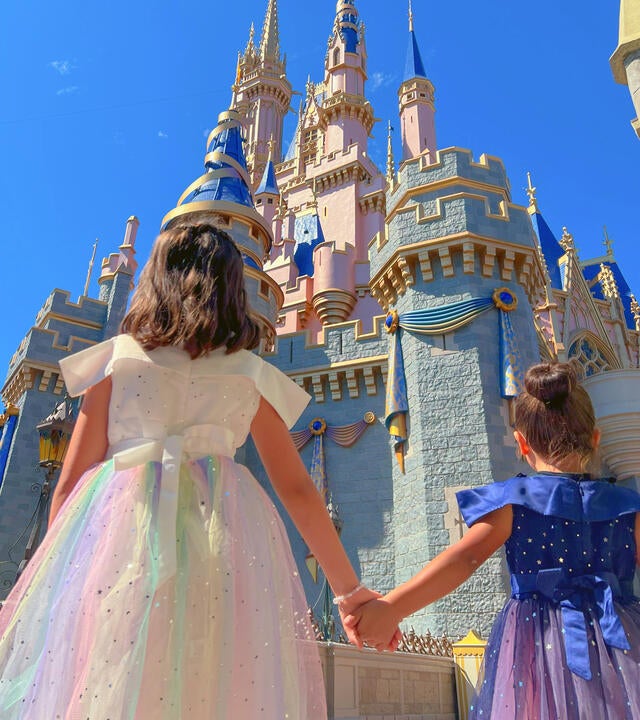 Giselle and sister Emily dressed as princesses holding hands facing away from the camera towards the caste at Walt Disney World