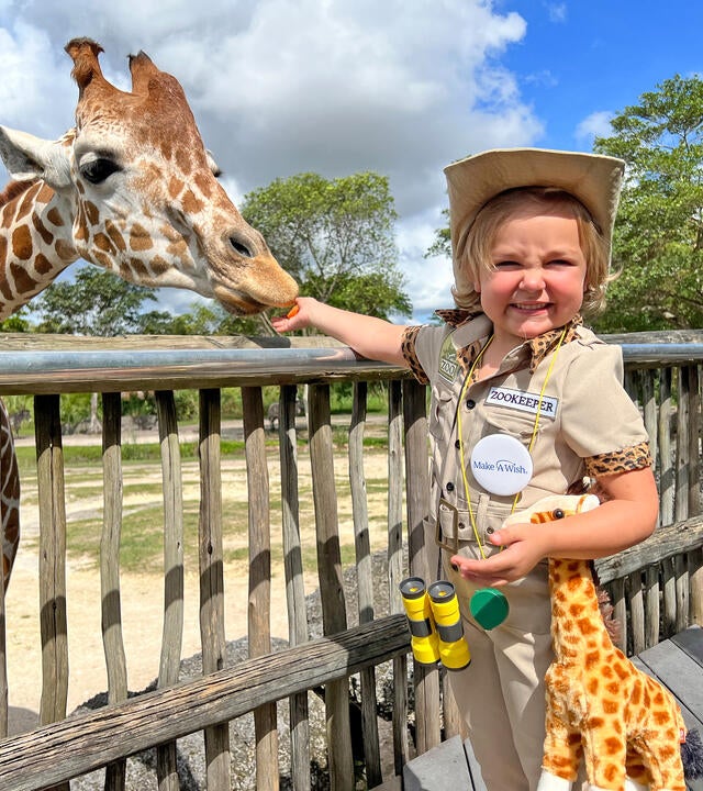 wish kid Amelia dressed in a zoo keeper feeding a giraffe