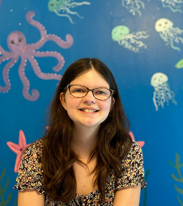 Addison smiles in front of a hospital wall that she painted