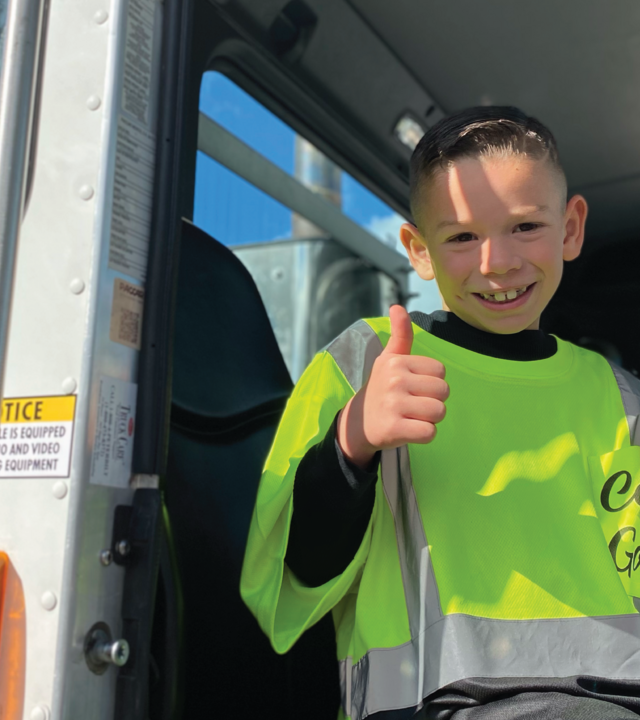 Carter sits in the garbage truck, giving a thumbs up