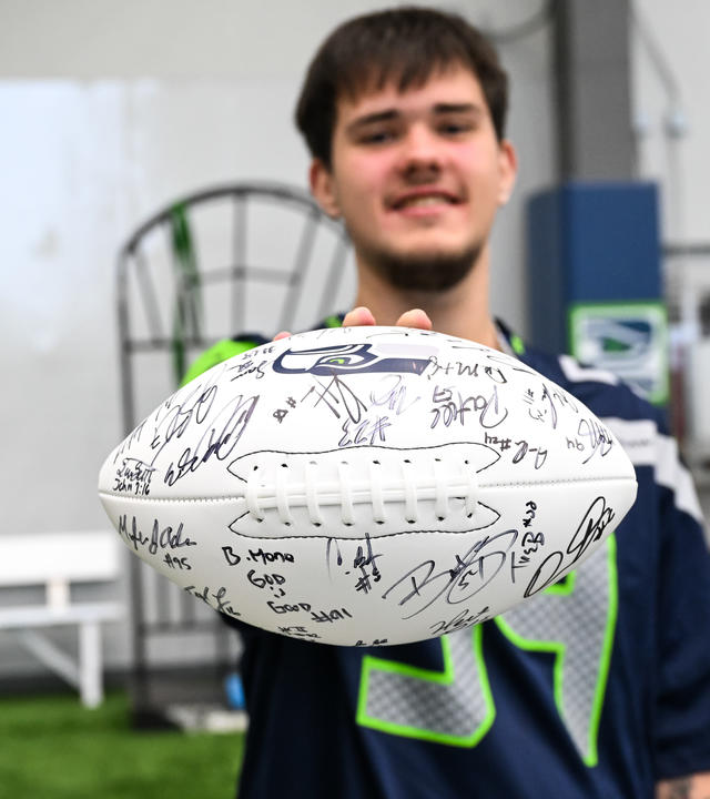 Wish kid Keegan holding signed football toward camera 