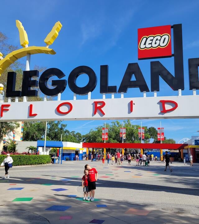 Wish kid Rowan smiling with excitement posing under the entrance sign for Legoland
