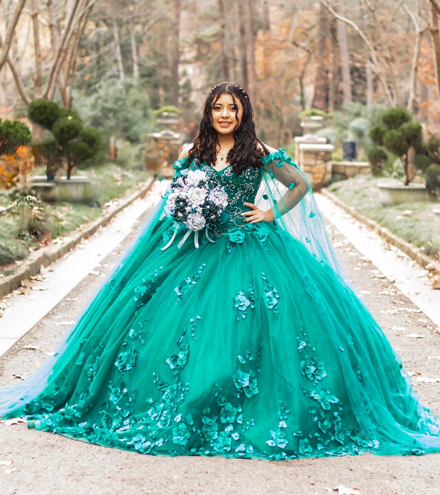 Wish kid Emely standing outside in a beautiful green ballgown holding a bouquet of flowers for her quinceanera
