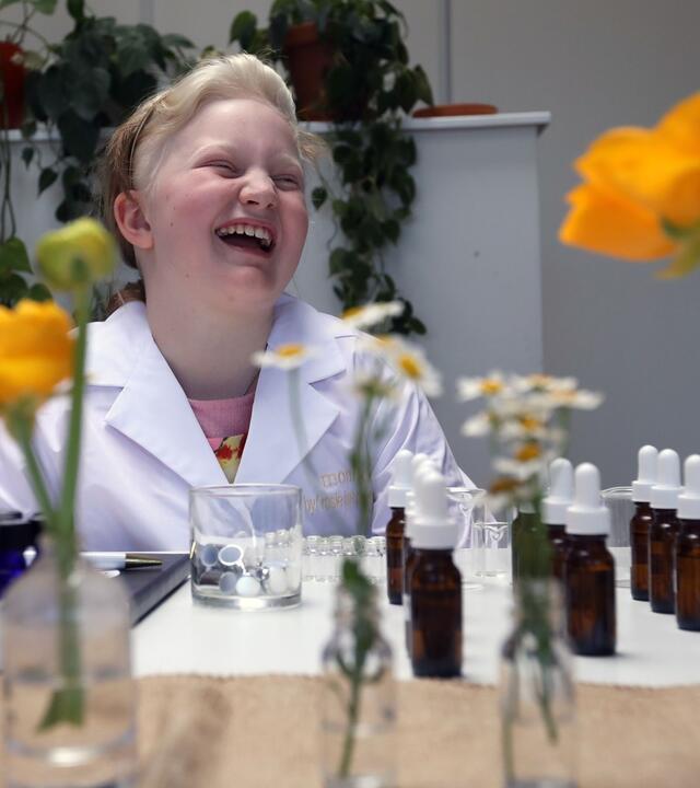 Monika smiling in the lab surrounded with fragrance bottles and yellow flowers