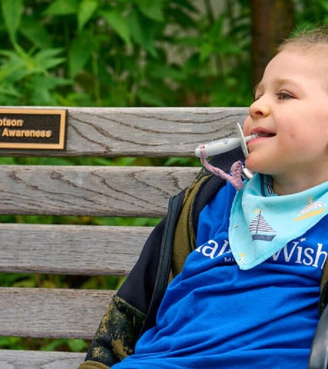 Derek sitting on his donated bench smiling with a plaque to honor him