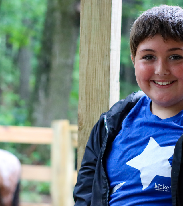 Maddie posed, smiling and wearing her Make-A-Wish star t-shirt, with horse in background