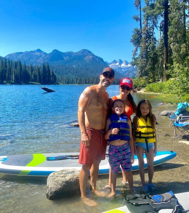 Family in swimming gear next to a boat by the water and the sun is shining.
