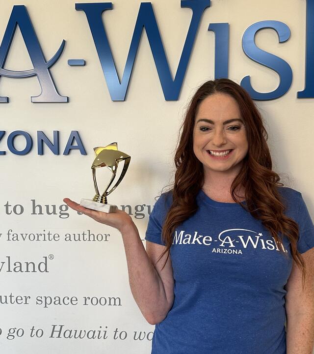 November of the month Amy Wilson standing by the Wish Wall with trophy