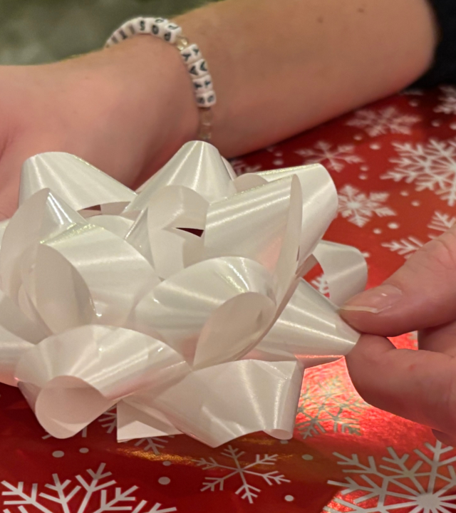 The hands of wish kid Emma, adding a bow to a wrapped holiday gift