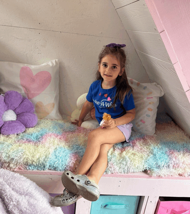 Tessa on a bench in her playhouse holding a doll
