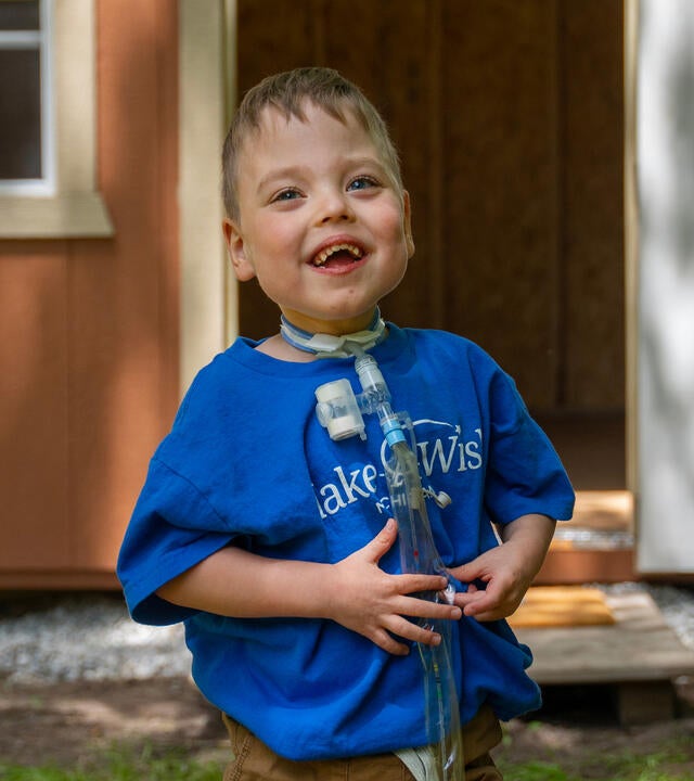 boy wearing blue Make-A-Wish shirt outside his playhouse