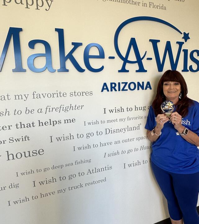January Volunteer of the month Michele Wexler standing by the Wish Wall with trophy