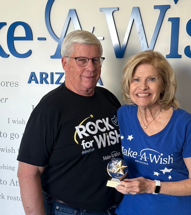 Pat and Bill Clemency standing by the Wish Wall smiling
