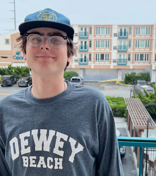 Aidan standing on a porch wearing a shirt that says "Dewey Beach"