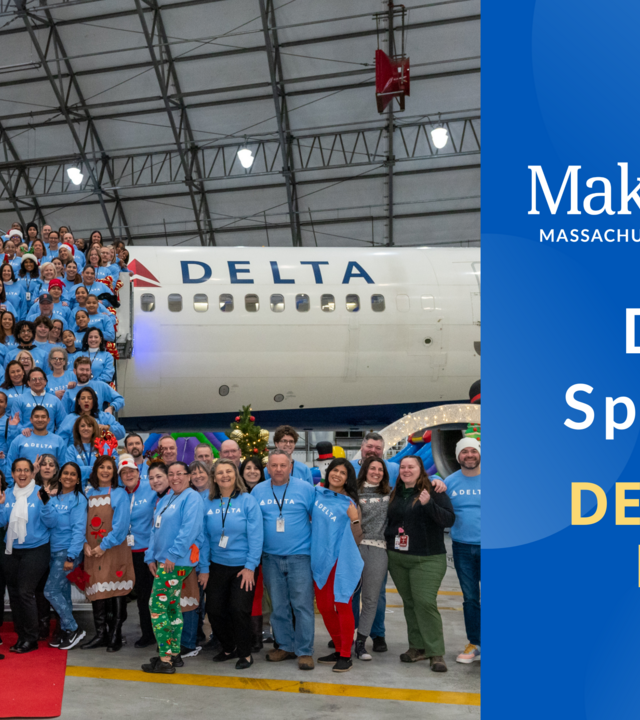 A photo of some of the Delta Air Lines employees at Logan Airport,posing in front of a plane in the Delta hangar