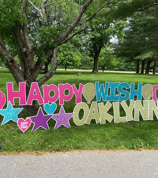 Oaklynn smiling next to a sign celebrating her wish day