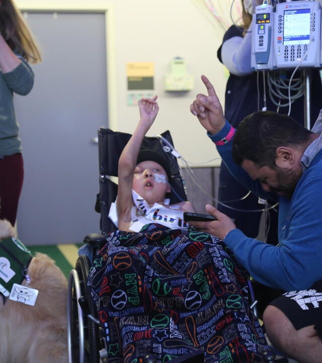 Neeno in a wheelchair at his birthday party wish, surrounded by his dad, a service dog, and a nurse