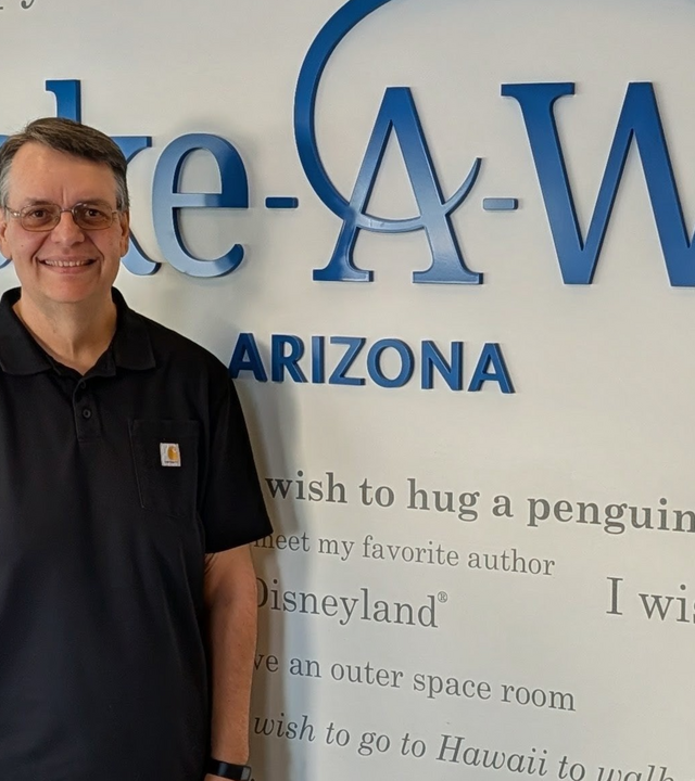 Eric Lardy, March Volunteer of the Month, in front of Wish Wall