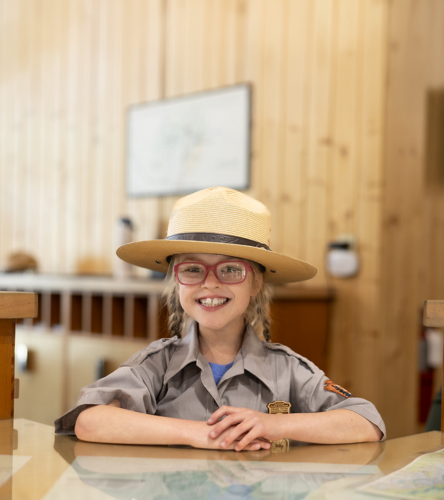 Wish kid Sammy sitting at a desk wearing a National Park Service ranger uniform