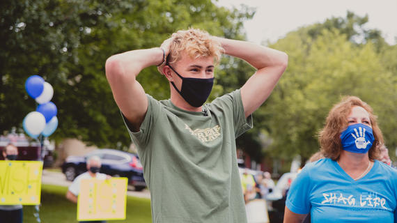Drew wearing a mask while he his surprised by volunteers with balloons and signs