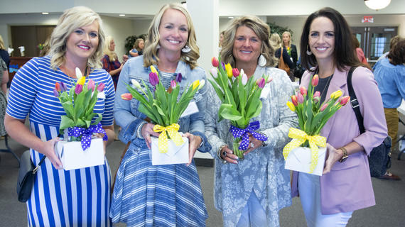 Four adults in business casual attire show off their multi-colored tulip arrangements.