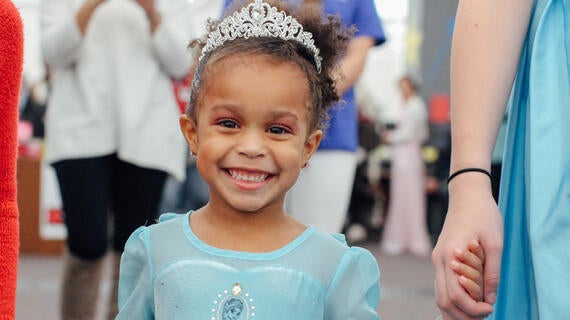 Sophia dressed as a princess holds that hand of a student volunteer