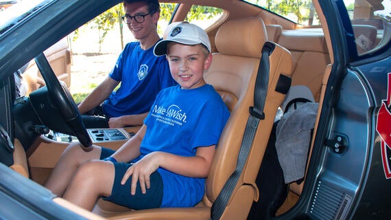 Wish kid in Make-A-Wish T-shirt in the drivers seat of a stopped car