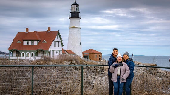 Adriana posando con su madre y hermano frente a un faro en Maine
