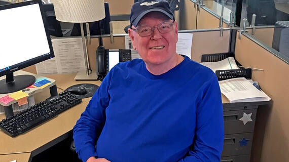 A Make-A-Wish Office Volunteer poses at his desk