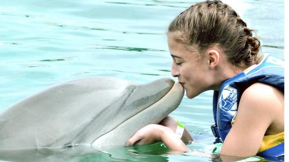 Picture of a wish kid kissing a dolphin. 