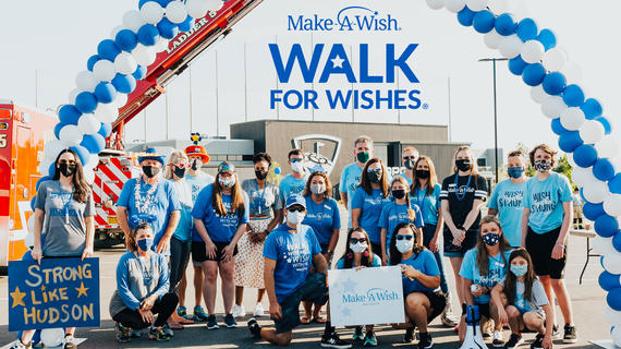 Group of people under a balloon arch and banner for Make-A-Wish Walk For Wishes event