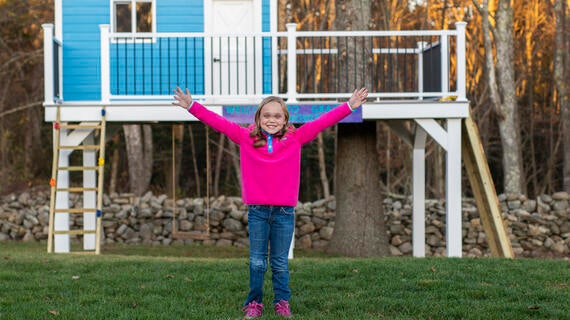 Gracie, 9, stands in front of her blue treehouse that she received for her wish.