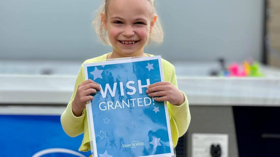 Wish child Kate in a yellow dress with a gemstone crown holding a "Wish Granted!" sign