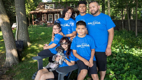 Johanna sits on a chair with her dog as she is joined for a photo with her mom and four other family members standing by her.