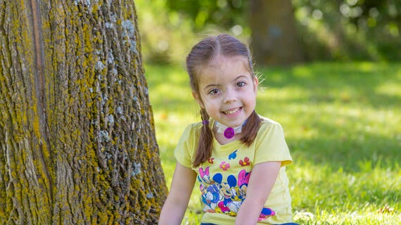 Wish kid Claire sitting by a tree smiling