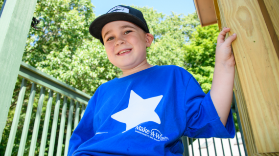 Wish kid Harrison in his Make-A-Wish blue t-shirt sitting on the porch of his treehouse