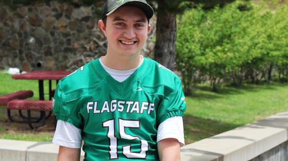 Stephen stands in front of his high school in his football uniform.