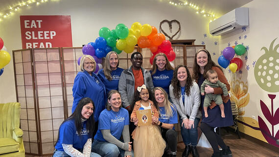 group smiling at camera with a rainbow balloon arch in the background.
