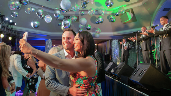 Man and woman taking a selfie with the live band on stage at WMP.