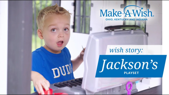 Young boy with blonde hair and a blue "DUDE" t-shirt looking surprised and playing a toy playset, sponsored by Make-A-Wish, with text that reads "Jackson's Playset."