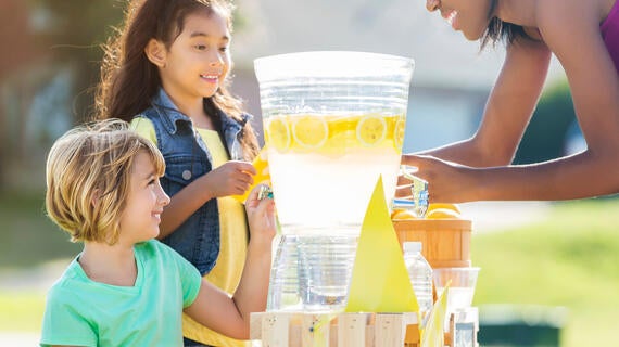 Two children sell lemonade to an adult