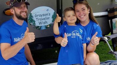 Grayson and his parents smile in front of his pop-up camper